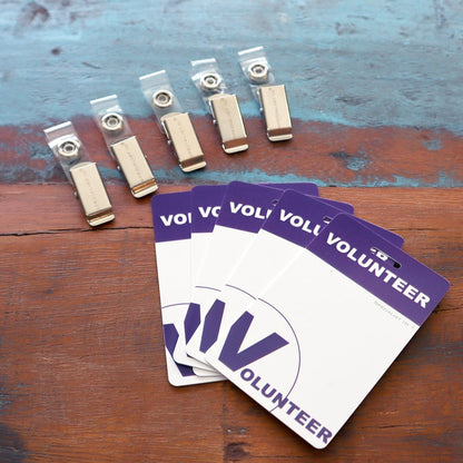 Five USB drives and four 5 Pack - Purple Heavy Duty Plastic Volunteer Badges with Clothing Friendly Clip are placed on a worn wooden surface.