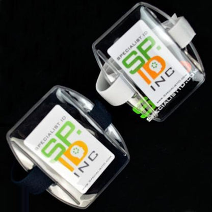 Two Government ID Size Vertical Arm Band Badge Holders with Heavy Duty Vinyl and Hook & Loop Elastic Bands (504-ARFB & 504-ARFW), one with a black strap and one with a white adjustable elastic strap, display government photo ID cards with the green, orange, and black logo of "Specialist ID, Inc." on a black background.
