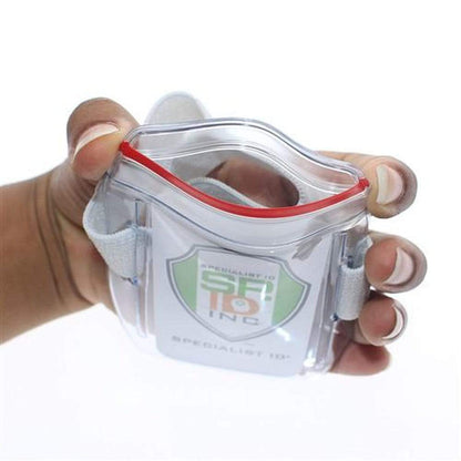A hand is holding a Vertical Armband ID Badge Holders with Zipper Top (504-ARZB & 504-ARZW) with a white card inside, featuring the text "Specialist ID Inc" and logo. The transparent plastic holder has adjustable white straps.