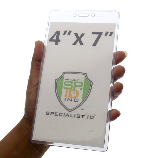 A hand holds an 4 1/8" X 7 1/2" Clear Vinyl Vertical Extra Large Badge Holder (P/N 506-4258) displaying a paper insert with the dimensions "4'' x 7''" and the "Specialist ID" logo.