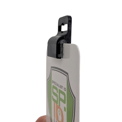 Close-up of a white and green identification badge with the logo "SPID" printed on it, secured by a Gripper 30 Card Clamp (P/N 5710-3050 Black & 5710-3058 White).