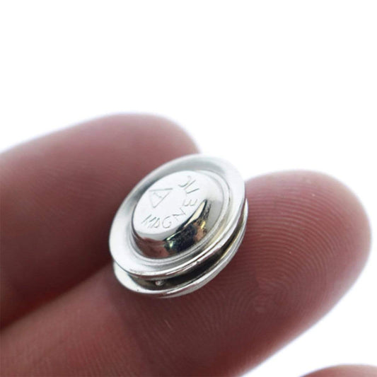 Close-up of a person's fingers holding a small, round silver magnetic snap clasp with "MAGNET" engraved on one side, ideal for securing a Magnetic Badge Finding, 1 Zinc-Plated Steel Encased Disc (P/N 5730-3030).