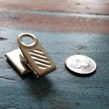 A Pressure-Sensitive Adhesive Back Nickel-Plated Clip, 1-Hole Ribbed Face (P/N 5735-2000), ideal for DIY projects, lies on a wooden surface next to a U.S. dime for size comparison.