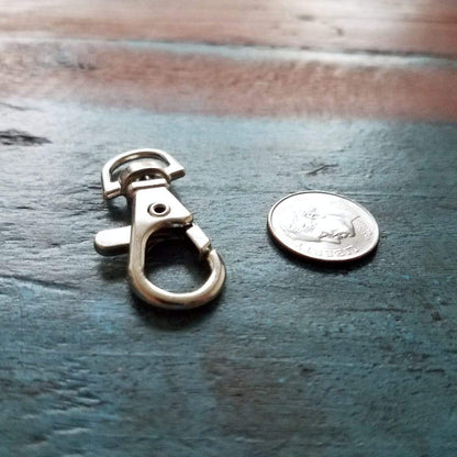 A Premium Metal Lobster Claw Clasp Hook Craft Findings - 1.5 Inch Clip with Trigger Snap and Round Eye Swivel D Ring is placed next to a quarter on a wooden surface, showcasing its potential for crafting and jewelry making.