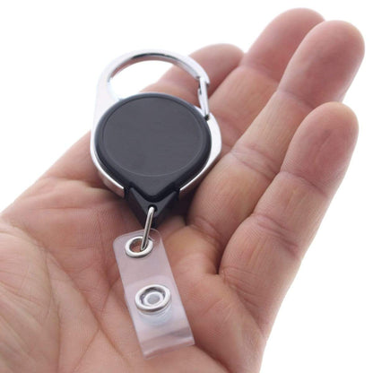 A hand holds a Carabiner No Twist Badge Reel (P/N 704-CB) with a retractable cord and a black face, featuring a clear plastic strap ending in a metal snap. Sold by Specialist ID.