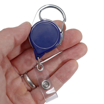 Hand holding a Carabiner No Twist Badge Reel (P/N 704-CB) with retractable cord, featuring a silver clip and clear strap with a no twist design. Sold by Specialist ID.