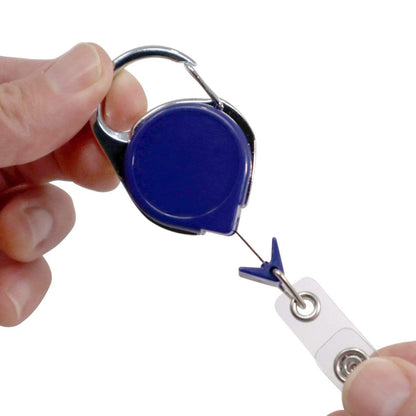 Person holding a Carabiner No Twist Badge Reel (P/N 704-CB) with a metal clip and extending the attached badge holder strap, featuring a retractable cord that ensures convenience and ease of use.