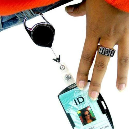 A person wearing an "OMG" ring is holding an ID card attached to a No Twist Badge Reel with Carabiner And Belt Clip (704-CLP), clipped to their jeans.