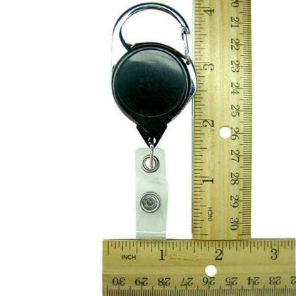 A No Twist Badge Reel with Carabiner And Belt Clip (704-CLP) is positioned next to a wooden ruler displaying inches and centimeters for scale.