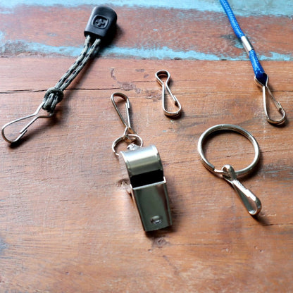 Various keychain accessories, including a whistle, ring, Small Metal J Hook Spring Clips - 1 1/4" for DIY Lanyards & Keychains (6920-2350), and straps for badge holders and ID cards, are spread out on a wooden surface.