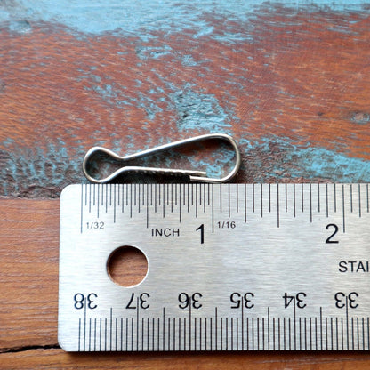 A metal ruler measuring approximately 2 inches is next to a Small Metal J Hook Spring Clips - 1 1/4" for DIY Lanyards & Keychains (6920-2350) and a badge holder on a wooden surface with a weathered, blue paint texture.