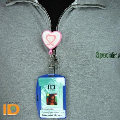 A SkimSAFE FIPS 201 RFID Blocking Single Card ID Holder (P/N AH-200) with a heart-shaped clip is attached to a gray zip-up jacket. The shielded card holder displays an ID with a photo and text, ensuring RFID blocking protection. The "Specialist ID" logo is visible at the bottom left corner, indicating it’s FIPS 201 approved.
