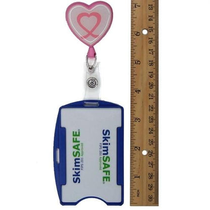 An ID badge holder with a blue clip and "SkimSAFE FIPS 201 RFID Blocking Single Card ID Holder (P/N AH-200)" printed on it, next to a 12-inch ruler and an RFID blocking retractable badge reel with a heart design.