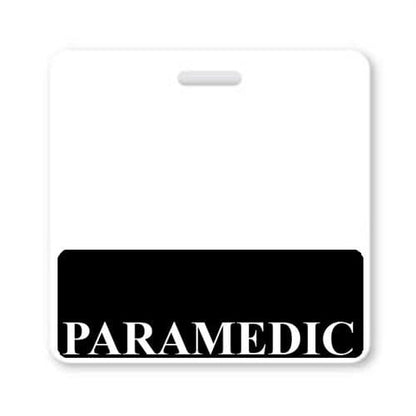 A rectangular badge with a white background and a black horizontal bar at the bottom displaying the word "PARAMEDIC" in large white letters, providing instant role recognition. Sold by Specialist ID.