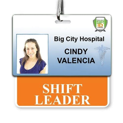 An ID badge showing Cindy Valencia from Big City Hospital, denoted as Shift Leader, with a photo of a woman in a blue shirt and a medical symbol in the background. The badge is printed on the highest quality synthetic paper for durability and role recognition, featuring the SHIFT LEADER Horizontal Badge Buddy with Orange Border.