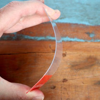 Close-up of a hand bending a thin, transparent plastic film over a wooden surface with a blue background, perfect for creating a Clear RN Badge Buddy Vertical with Color Border for Registered Nurses - Double Sided Print.