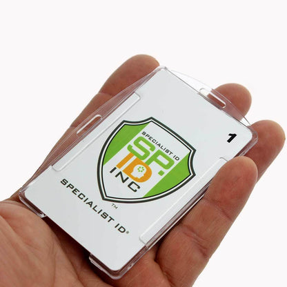 A hand holds a Specialist ID badge, encased in a Crystal Clear Rigid Open-Faced Single ID Card Holder (P/N SPID-075) made from sturdy polycarbonate material. The badge features the letters "SP" and "ID" in green and yellow colors and is labeled "1," with adaptable slot holes for easy attachment.