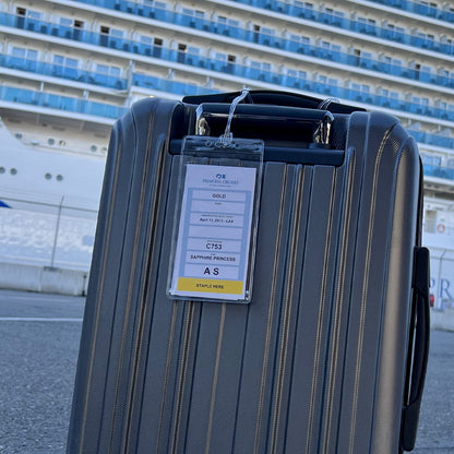A close-up of a hard-shell suitcase in front of a cruise ship. The suitcase has a luggage tag held securely in Premium Vinyl Cruise Ship Luggage Tag Holders with 9" Worm Loops Attach to Your Suitcases, Bag Handles, and Carry On Luggage - 3 1/2 x 7" Clear Protective Insert Sleeves by Specialist ID, indicating "Gold" status, the date "April 14, 2011 - LAX," and the cabin number "C753 Sapphire Princess S".