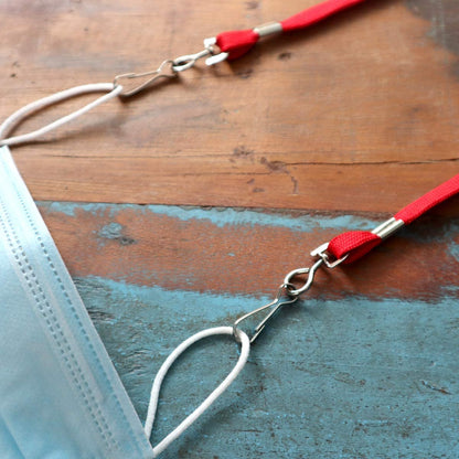 A blue face mask is attached to a red lanyard with Premium Metal Swivel J Hook Clips with 1/2 Inch D Ring - Great for DIY Lanyards & Crafts (6920-2300), lying on a wooden surface with peeling paint.