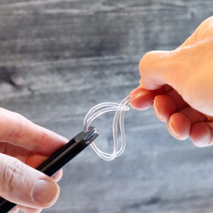 Close-up of two hands holding a black device and a transparent loop tool against a blurred background, showcasing 2 Pack - Heavy Duty Medical Equipment Luggage Tags CPAP / BIPAP with Plastic Loops.