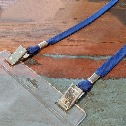 A close-up of a Double-Ended Lanyards with Bulldog Clips on Each Side - Comfort Neck Straps ID Holder for Special Event Badges clipped to a clear plastic badge holder lying on a wooden surface.