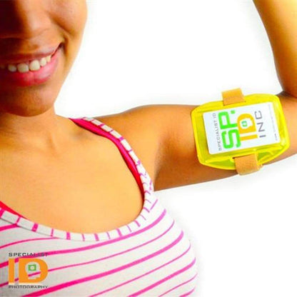 A woman wearing a striped tank top smiles while displaying a Vertical Reflective Armband ID Holder (R504-ARN) with an adjustable strap and a visible identification card.