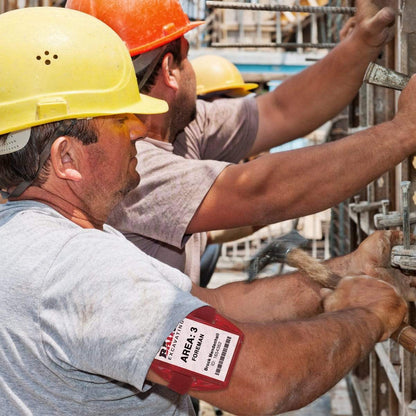 Construction workers wearing helmets and Vertical Reflective Armband ID Holder (R504-ARN) work together on a building site, each holding a tool to secure materials.