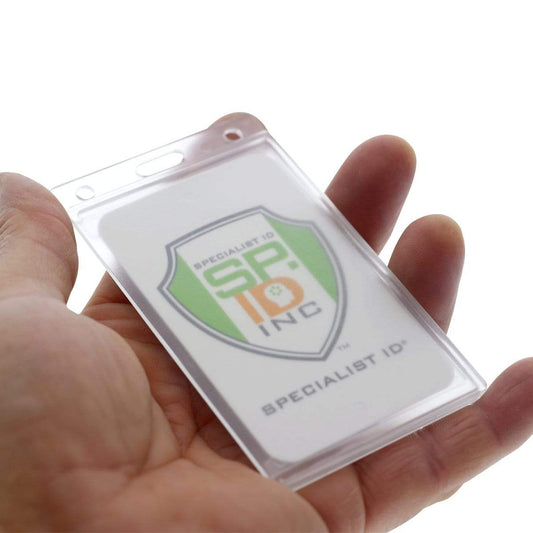 A hand holding a clear plastic Side Load Slim Rigid Plastic Badge Holder with Thumb Notch (1840-6500) containing a card labeled “Specialist ID, Inc.” with a green and orange shield logo.