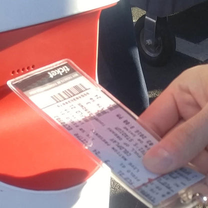 A person's hand holds a Clear Ticket Holder for 2 1/8 X 5 5/8 Inch (Ticketmaster Size) Concert and Sporting Event Tickets & Credentials (SPID-1140) with a barcode, inserting it into a red and white ticket machine, similar to how one would use sporting event tickets for entry.