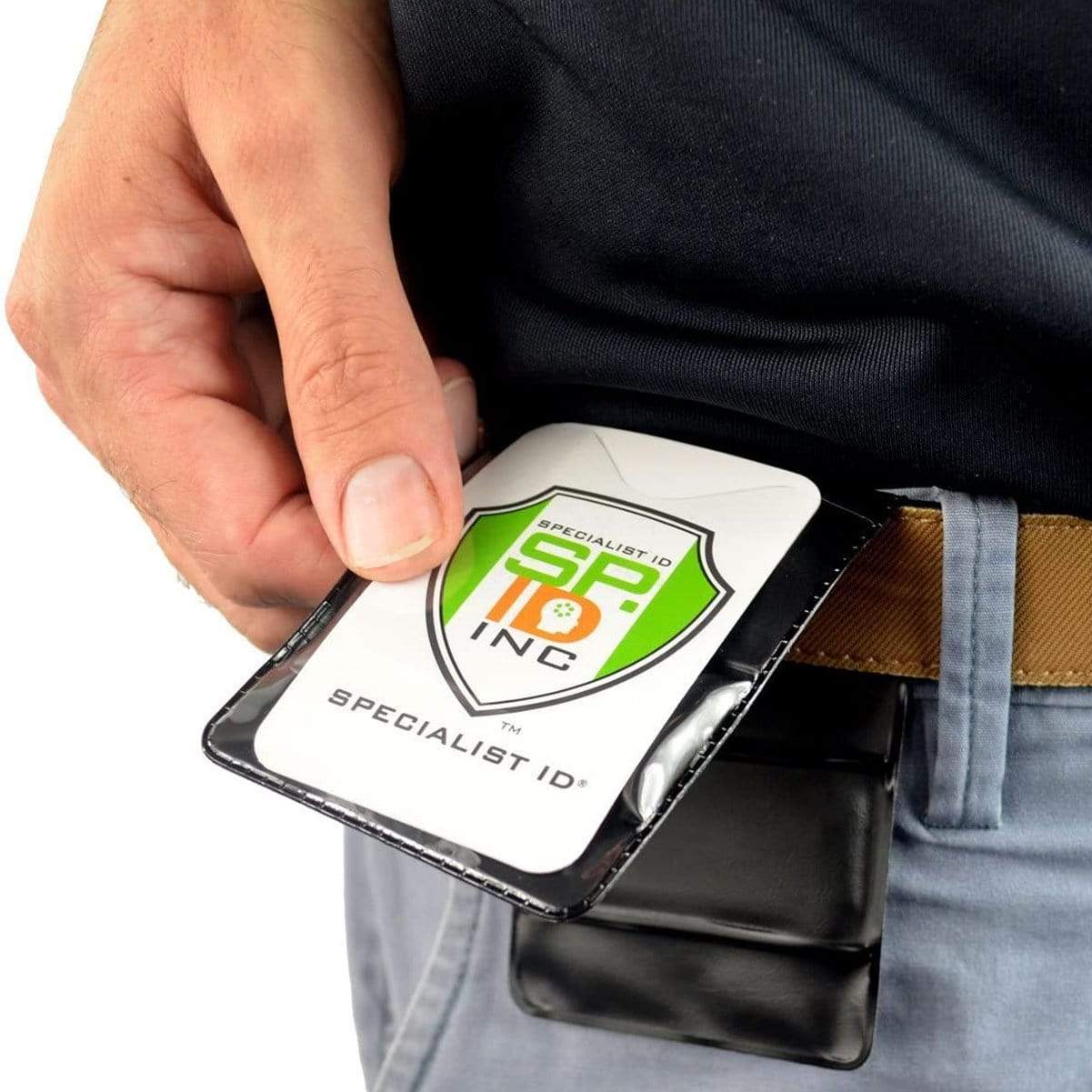 Close-up of a person holding a Specialist ID badge with a green and orange logo, attached to a Magnetic Vertical Double Pocket Badge Holder (1835-1115) on their belt. The person is wearing blue pants and a black shirt.