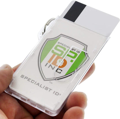 Close-up of a hand holding a Two Card Vertical Clear Rigid Plastic Fuel Card and Badge Holder with Keychain (SPID-1220) with a Specialist ID Inc badge visible inside, displaying a green shield logo and the text "SPECIALIST ID." A keyring is attached to the badge holder.