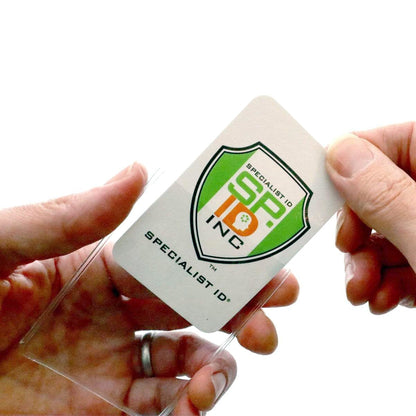 Two hands are inserting a white Specialist ID, Inc. badge into a Clear Vinyl Business Card Holder - Medicare Card Protective Sleeve (1840-3505) against a white background.