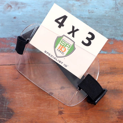 An Armband Badge Holder Horizontal - 4" X 3" Name Badge Holder with Adjustable Arm Band lies on a wooden surface, showcasing a white card displaying "4 x 3" alongside the Specialist ID logo.