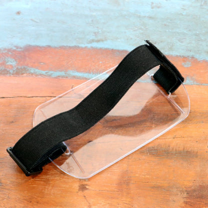A transparent Armband Badge Holder Horizontal - 4" X 3" Name Badge Holder with Adjustable Arm Band is placed on a wooden surface. Sold by Specialist ID.