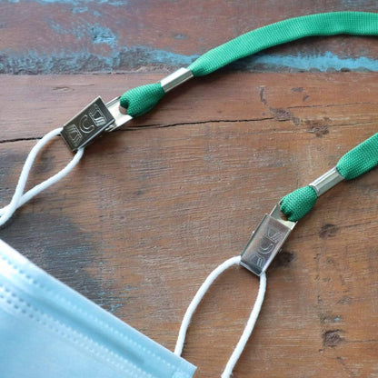 Close-up of a face mask with green straps attached to the ear loops, reminiscent of Double-Ended Lanyards with Bulldog Clips on Each Side - Comfort Neck Straps ID Holder for Special Event Badges, resting on a wooden surface.