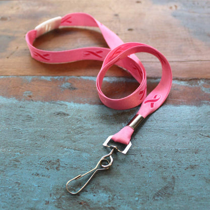 A Pink Ribbon Awareness Wide Flat Breakaway Lanyard w/ Swivel Hook 2138-5286 is laid out on a rustic wooden surface.