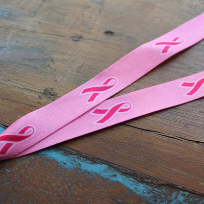 A Pink Ribbon Awareness Wide Flat Breakaway Lanyard w/ Swivel Hook 2138-5286 lying on a wooden surface.