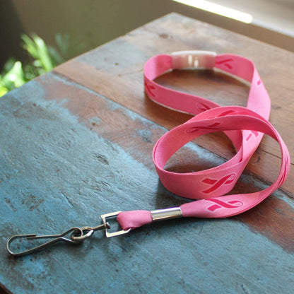 A Pink Ribbon Awareness Wide Flat Breakaway Lanyard w/ Swivel Hook 2138-5286, designed for breast cancer awareness, rests on a wooden surface.