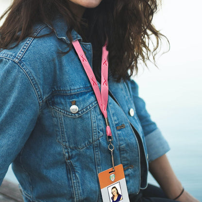 A person with wavy hair wearing a denim jacket and a Pink Ribbon Awareness Wide Flat Breakaway Lanyard w/ Swivel Hook 2138-5286 holding an ID badge is sitting outdoors near water.