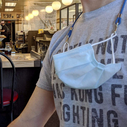 A person in a gray t-shirt with a face mask hanging around their neck, sitting inside a diner with globe lights, showing off an Adjustable Length Double Ended Lanyard - Handy & Convenient Event Badge Holder & Hanger with 2 Clips at the counter with condiments and a man in the background.
