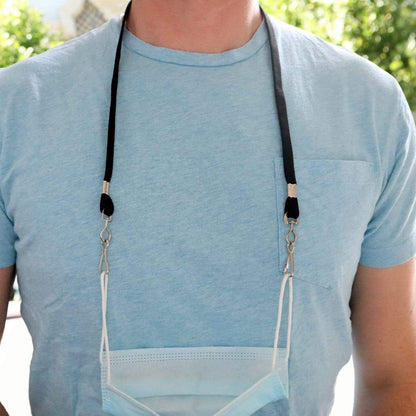 A person wearing a blue shirt is shown with a Face Mask Lanyard / Hanger with Safety Breakaway Clasp - Ear Saver with J Hooks Adult Size around their neck, holding a blue surgical mask hanging in front of them.