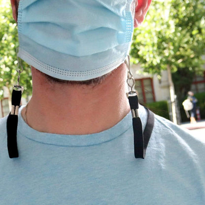 A person wearing a blue surgical mask with black eyeglass straps and a Face Mask Lanyard / Hanger with Safety Breakaway Clasp - Ear Saver with J Hooks Adult Size attached to it, outdoors on a sunny day.