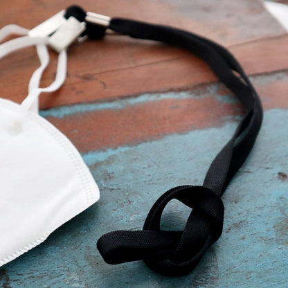 Close-up of a white face mask and a black, knotted lanyard resting on a worn, blue and brown wooden surface, featuring a 5 Pack Double Ended Lanyards with Bulldog Clips - Comfortable Premium Economy Neck Strap Badge Holder for Events.