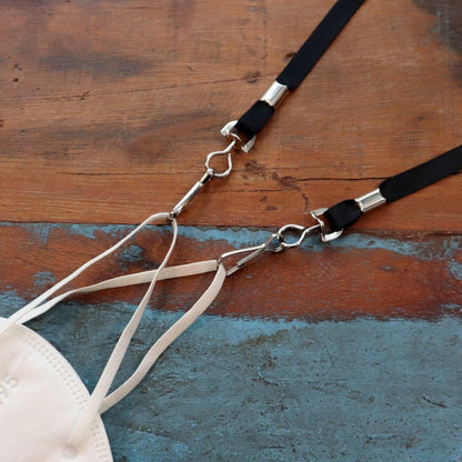 A white face mask with beige straps, featuring germ-inhibiting nanoparticle-coated fibers, is connected to an Antimicrobial Lanyard with Two Clips - Short Length Double Clip Lanyard with Safety Breakaway - 25 Inch Perfect Size for Students & Adults (SPID-2360), placed on a wooden surface.