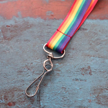 A **Rainbow Lanyard with Breakaway Clasp and Swivel Hook (P/N 2138-5260)** lies on a weathered blue surface.