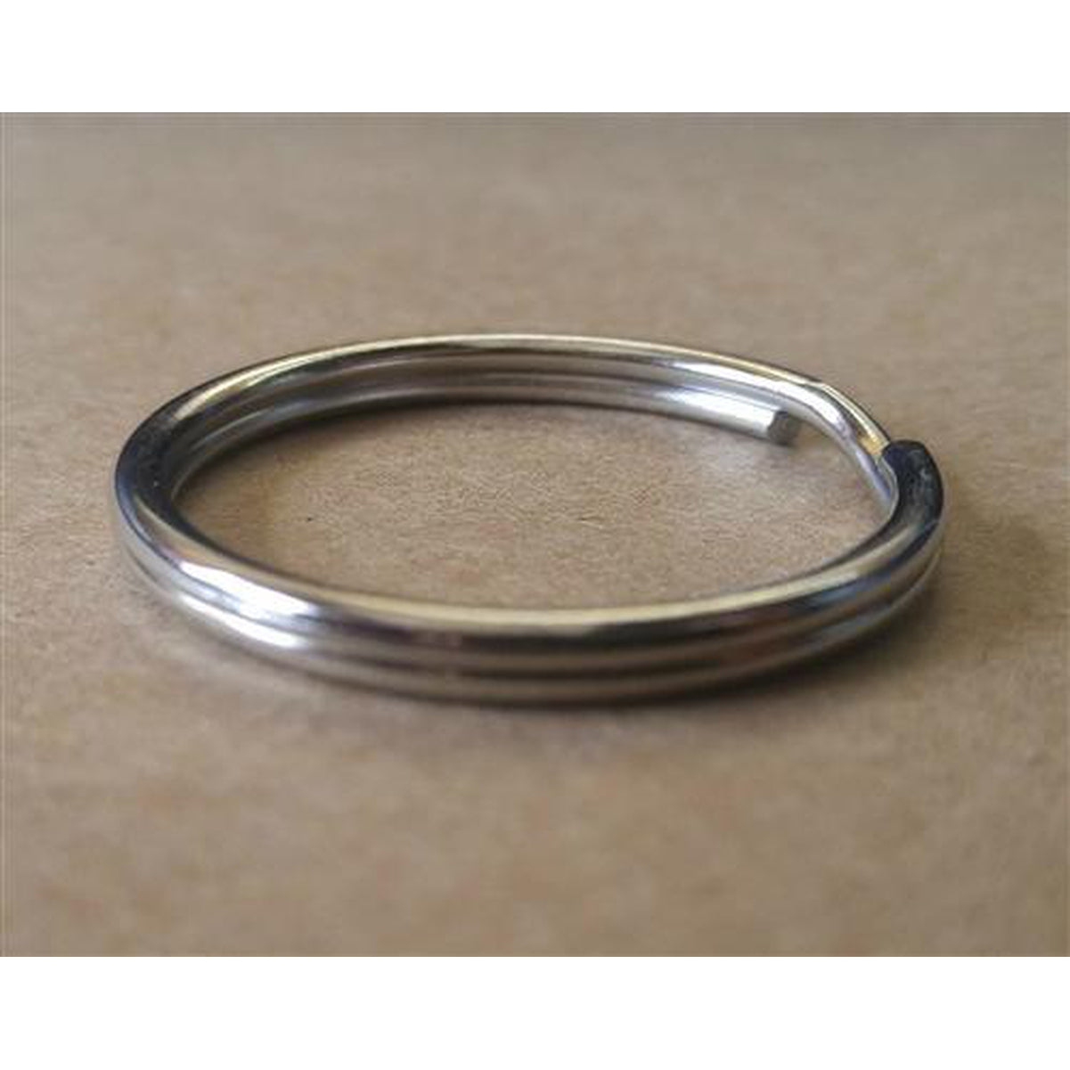 A close-up image of a 25 Premium Extra Large 1 1/4" Split Rings (SPID-9240), crafted from heat treated steel, lying on a beige surface.