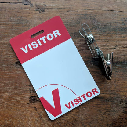 Reusable Visitor Passes with Clothing Friendly Badge Clip featuring a red and white design alongside a metal clip on a wooden surface, perfect for use with dry-erase markers.