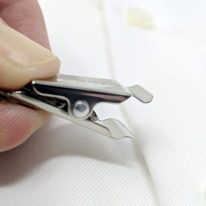A hand uses a metal tool with a sharp tip to remove a plastic tag from a white garment, much like carefully detaching Reusable Visitor Passes with Clothing Friendly Badge Clip after an event.