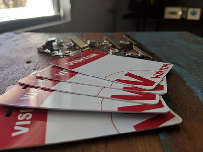 Reusable Visitor Passes with Clothing Friendly Badge Clip are placed on a wooden table near a window, alongside a dry-erase marker for easy updating.