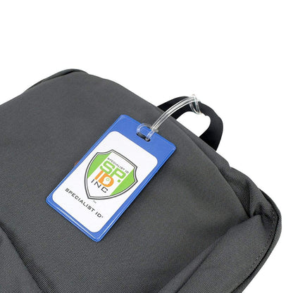 A close-up of a gray backpack features an attached blue-and-white luggage tag labeled "Specialist ID, Inc." secured with Clear Plastic Luggage Loop Straps 6 Inch - Durable Worm Loops (2410-2000).